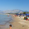 Spiaggia affollata con ombrelloni blu e montagne.