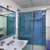 Bagno con box doccia a mosaico blu e lavabo bianco.
