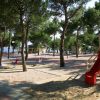 Parco giochi tra gli alberi con scivolo rosso e giochi a molla.