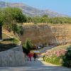 Due persone camminano su un sentiero verso una spiaggia, circondate da colline.