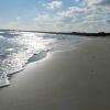 Una spiaggia deserta con il mare calmo e il sole che riflette sull'acqua.