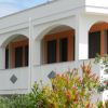 Facciata di edificio bianco con archi e cespugli fioriti.