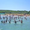 Un gruppo di persone si diverte in mare, con la spiaggia piena di ombrelloni sullo sfondo.