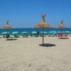 Spiaggia con capanne di paglia e ombrelloni verdi, persone rilassate in riva al mare.