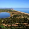 Paesaggio costiero con lago, spiaggia e vegetazione lussureggiante.