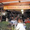 Ristorante pizzeria all'aperto con tavoli occupati da clienti.
