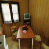 Cucina con tavolo marrone, due sedie, TV su scaffale, e lavello. Camera da letto visibile.