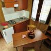 Piccola cucina con tavolo di legno, sedie, mini frigo, lavandino, fornelli e TV su mensola.