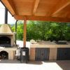 Barbecue e cucina esterna sotto un pergolato con vista verso il verde.