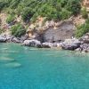 Una scogliera rocciosa con vegetazione fitta si affaccia su un mare turchese limpido.