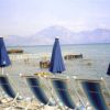 Spiaggia con sedie a sdraio blu e ombrelloni, vista sul mare e montagne sullo sfondo.