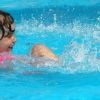 Bambina che gioca e sorride in una piscina, spruzzando acqua.