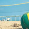 Palla da beach volley su sabbia con rete sfocata.