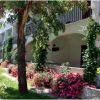 Edificio bianco con balconi e giardino verde, fiori rosa e piante rampicanti.