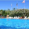Piscina all'aperto con sedie a sdraio, bandiere e alberi sullo sfondo.