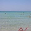 Mare azzurro trasparente con alcune persone che nuotano. Cielo sereno sullo sfondo.