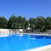 Una piscina all'aperto circondata da alberi e lettini, sotto un cielo blu.