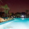 Piscina illuminata di notte tra palme e rocce.