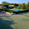 Campo da tennis all'aperto con persone che giocano; piscina e giardini vicini.