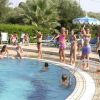Persone intorno a una piscina, alcune in piedi, altre in acqua.