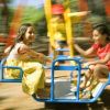 Tre bambini sorridenti su una giostra girevole in un parco giochi.