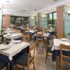 Ristorante con tavoli apparecchiati, sedie di legno e grandi finestre che illuminano l'ambiente.