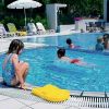 Bambini che giocano in piscina, circondati da sdraio e ombrelloni.