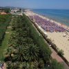 Spiaggia affollata con ombrelloni viola, vista dall'alto.