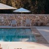 Piscina con sedie e ombrelloni vicino a muro di pietra.