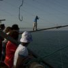 Persone osservano un uomo camminare su travi sopra il mare.