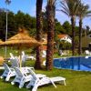 Piscina all'aperto con sdraio bianche e ombrelloni di paglia tra palme.