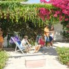 Persone in giardino con sedie a sdraio sotto un pergolato fiorito.