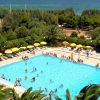 Piscina affollata con ombrelloni gialli, circondata da vegetazione verde.