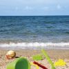 Secchiello e palette sulla sabbia di una spiaggia con il mare sullo sfondo.