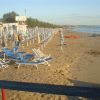 Una spiaggia con file di lettini e ombrelloni blu e bianchi lungo la costa.