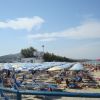 Spiaggia affollata con persone su lettini sotto ombrelloni blu e bianchi.