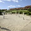 Spiaggia sabbiosa con ombrelloni chiusi, villette sullo sfondo.
