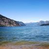Vista di un lago con acque calme, montagne verdi e cielo sereno.