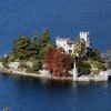 Piccola isola con un castello circondato da alberi e acqua blu.