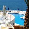 Una piscina a sfioro con vista sul mare, circondata da lettini e ombrelloni blu.