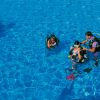 Tre persone con attrezzatura subacquea in una piscina azzurra, una persona sta assistendo le altre.