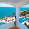 Una terrazza con vista sul mare e due piscine all'aperto, circondate da sedie a sdraio colorate.