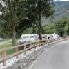 Una strada con camper parcheggiati accanto a un prato verde e alberi, con montagne sullo sfondo.