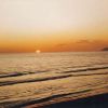 Tramonto sul mare con onde leggere e profilo di una montagna all'orizzonte.