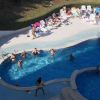 Gruppo di persone nuota in una piscina, altre prendono il sole su sdraio.