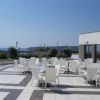 Una terrazza con tavoli e sedie bianche, vista mare e cielo sereno.