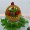Un melone intagliato a forma di cestino con pomodori e insalata, su un vassoio bianco.