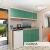 Cucina compatta con mobili verdi e un piccolo frigorifero, accanto a una porta aperta.