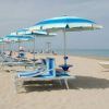 Spiaggia con ombrelloni e lettini blu su sabbia chiara, mare calmo sullo sfondo.