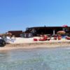 Spiaggia con barca sulla sabbia, molti ombrelloni e bagnanti in acqua.